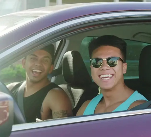 Two young men smiling at the camera inside a car.